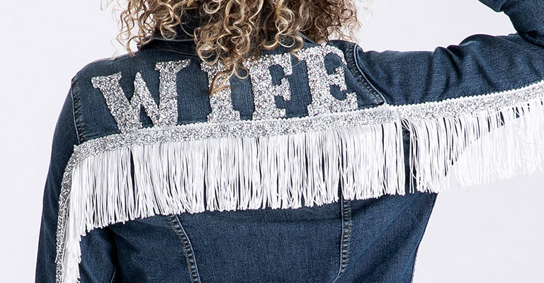 Woman with blonde hair wearing a denim blue jacket with white fringe that says wife in rhinestones