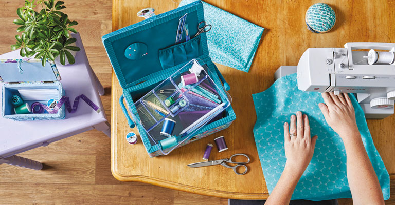 hands sewing blue fabric with a sewing machine surrounded by other dewing supplies